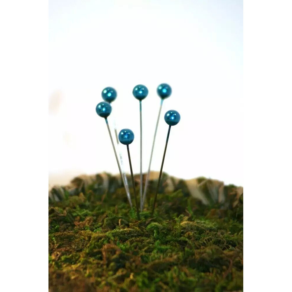 Épingles à tête perle nacrée bleu turquoise piquées dans de la mousse pour décoration florale de fleuriste
